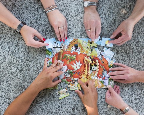 Viele Hände bauen ein Puzzle zusammen